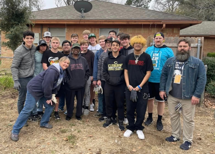 Group of people standing together outdoors in front of a brick house, posing for a photo.